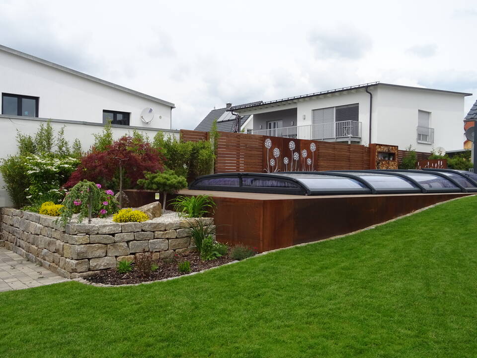 Sichtschutz für einen Garten-Pool: Abwechselnd weiße Mauer, Holz-Paneele und Cortanstahl mit Blumenelementen.