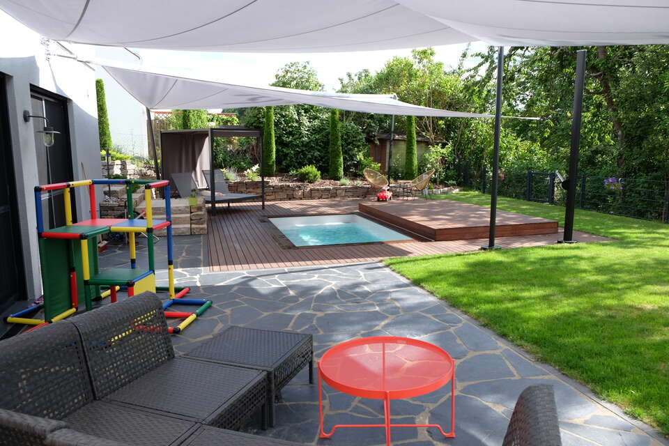 Gartengestaltung mit Terrasse und Pool, Pooldeck, weißem Sonnensegel, Schattenliege, Outdoor-Lounge sowie rotem Outdoor-Couchtisch in Langenzenn bei Nürnberg