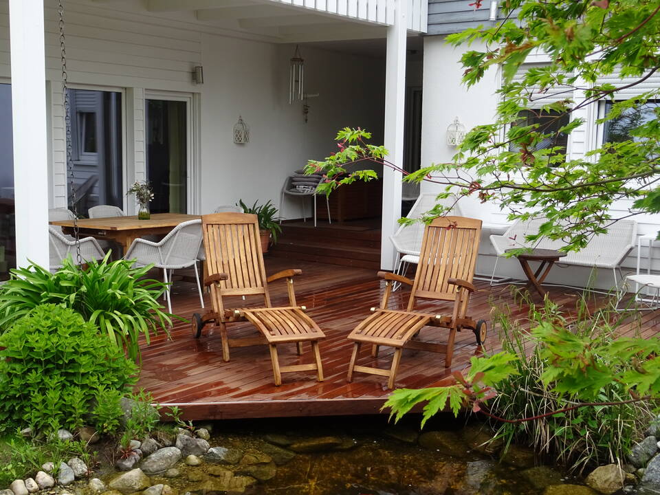 Hölzerne Terrasse mit Gartenmöbeln in einer Ecke eines Ansbacher Hauses. Davor ein Gartenteich.