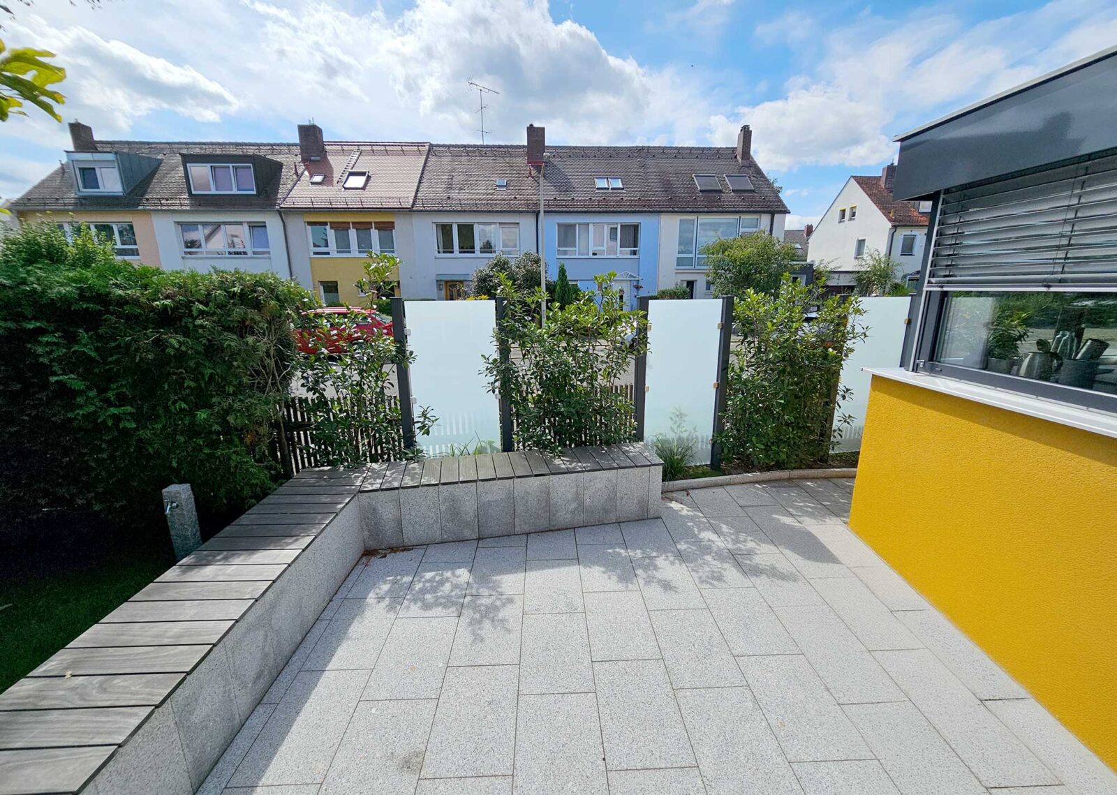 Hölzerner Gartenzaun mit Hecke, unterbrochen von Sichtschutz-Elementen aus Milchglas.