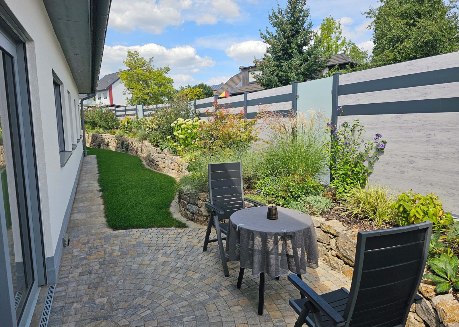 Sichtschutz aus WPC-Platten mit Holzoptik und grauen Streifen, unterbrochen von satinierten Glasscheiben als Gartenzaun.