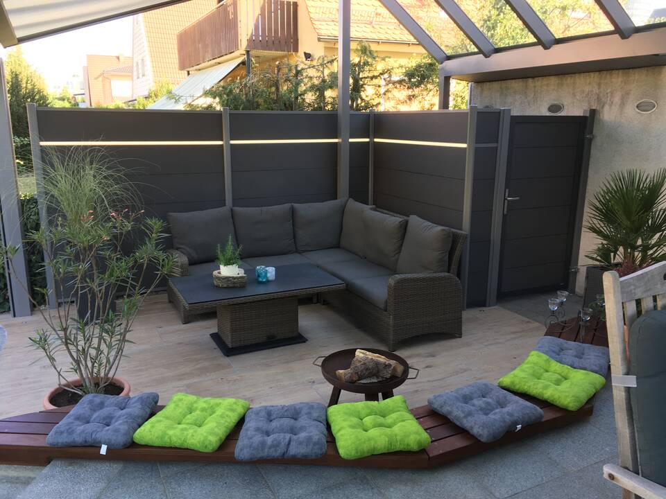 Garten-Lounge auf der Terrasse mit gläsernem Terrassendach und dunkelgrauem HPL-Sichtschutz inkl. Gartentür.