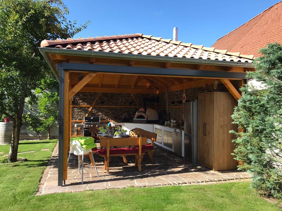 Gartenküche mit Überdachung und Gartentisch in einem Garten in Nürnberg, schön zu erkennen: Der eigene Kamin für den Pizza-Ofen