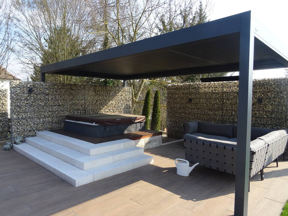 Garten-Lounge mit grauem Garten-Sofa und Whirlpool mit weißen Stufen unter einem Lamellendach