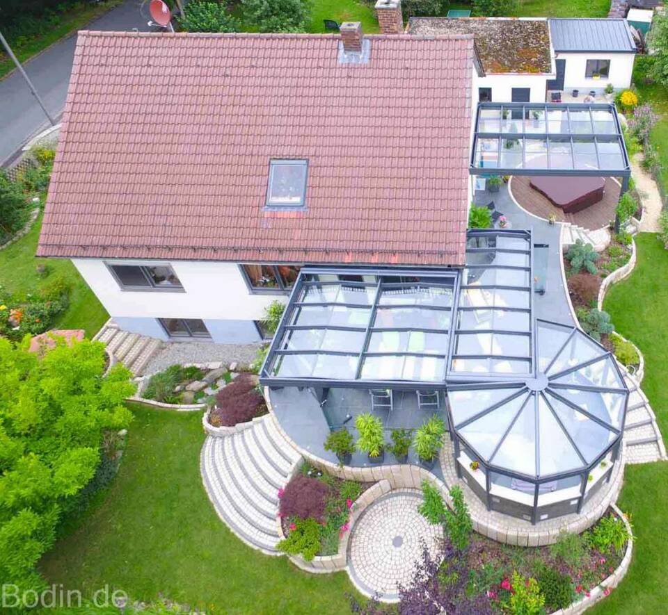 Luftbild von Haus und Terrasse: Vorne überdachte Outdoor-Küche und Sommergarten, im Hintergrund der Whirlpool mit Dach.