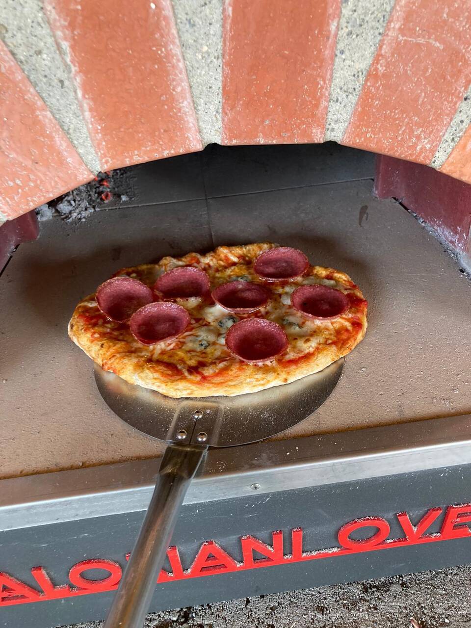 Holzofen-Pizza, die direkt aus dem Pizza-Ofen einer Outdoorküche mit Überdachung kommt.