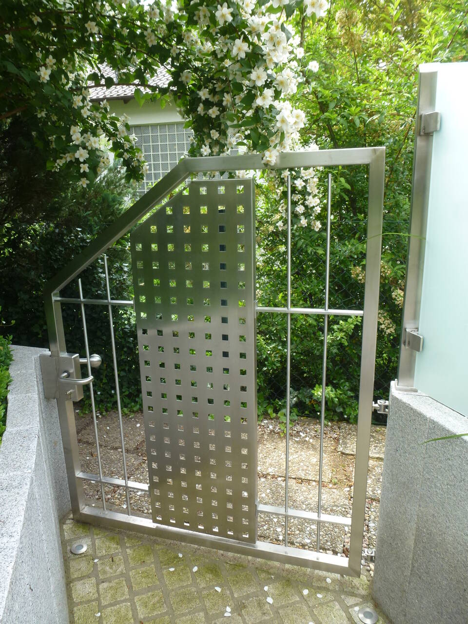 Edelstahl-Gartentür mit Lochblende, daneben eine Sichtschutz-Wand aus Glas.