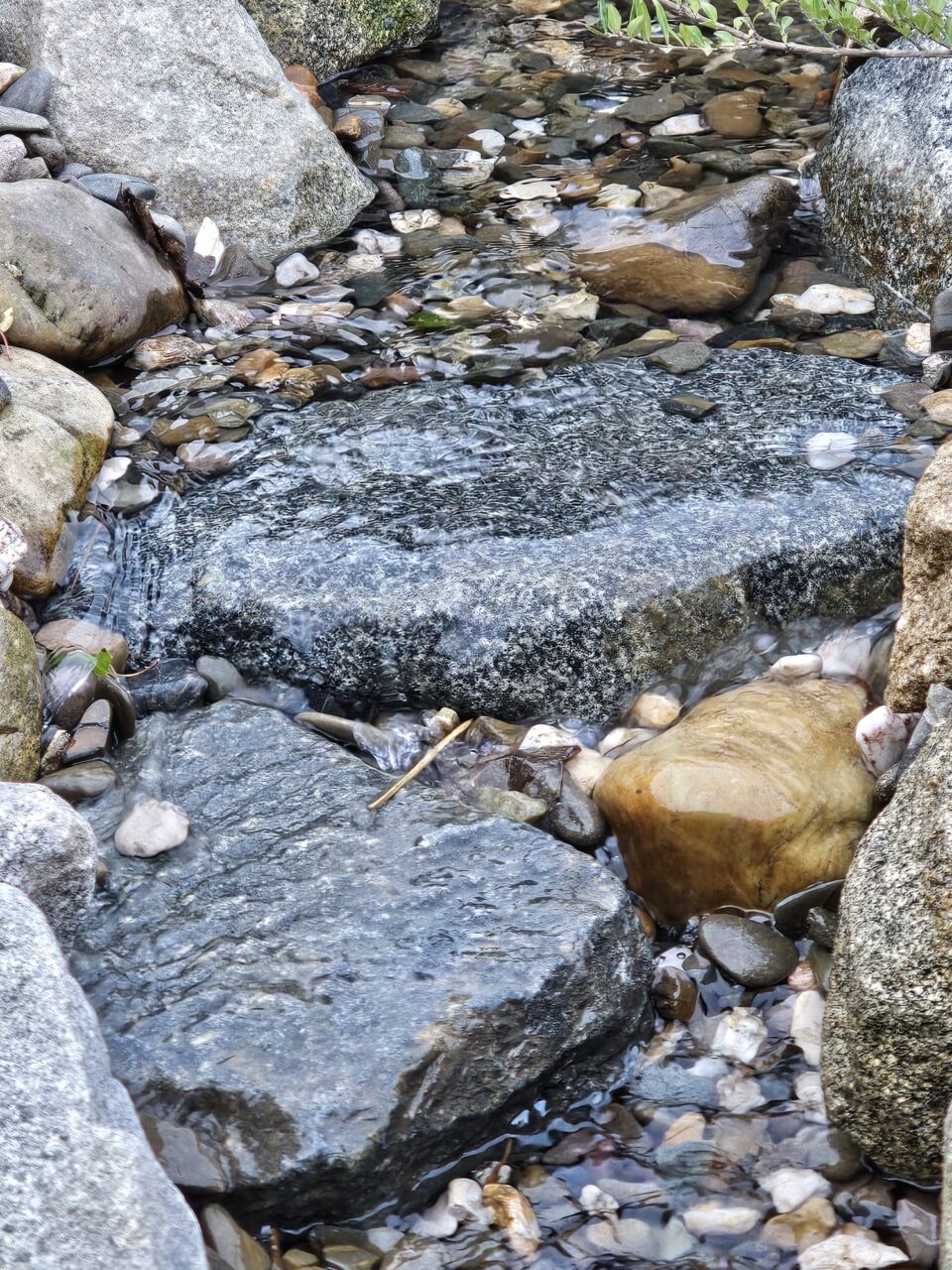 Ein Bachlauf um Garten fließt über verschiedene Natursteine.