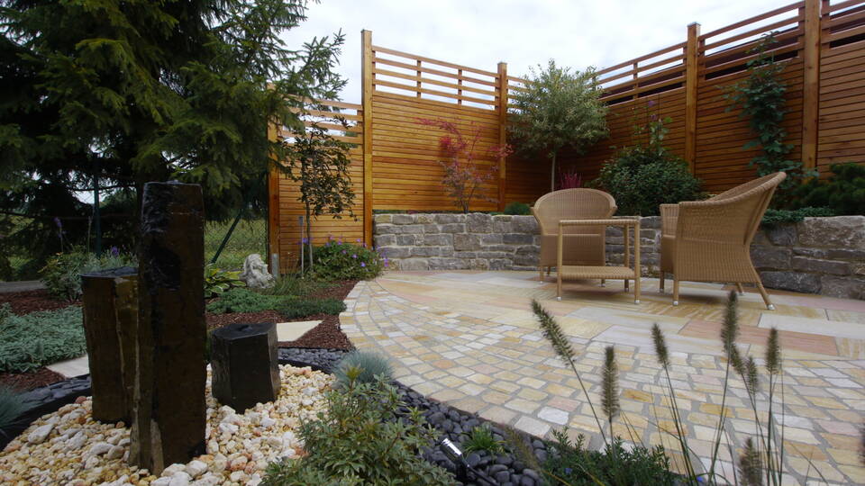 Sitzecke mit Sichtschutz aus Holz, daneben Maschendrahtzaun